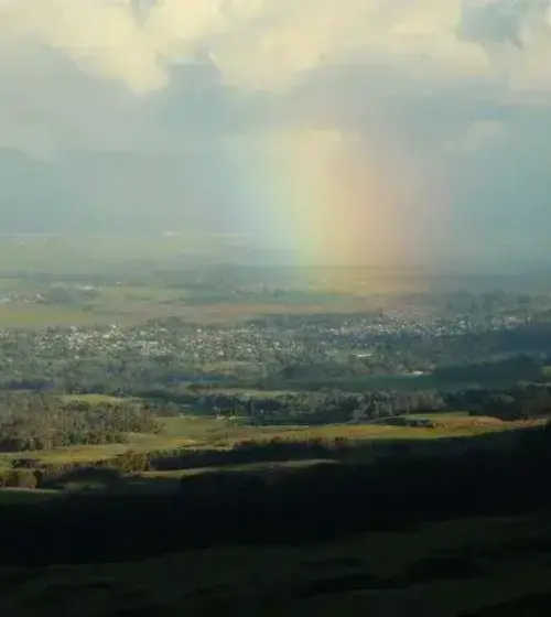 Rainbow appearing over a rural landscape with scattered clouds