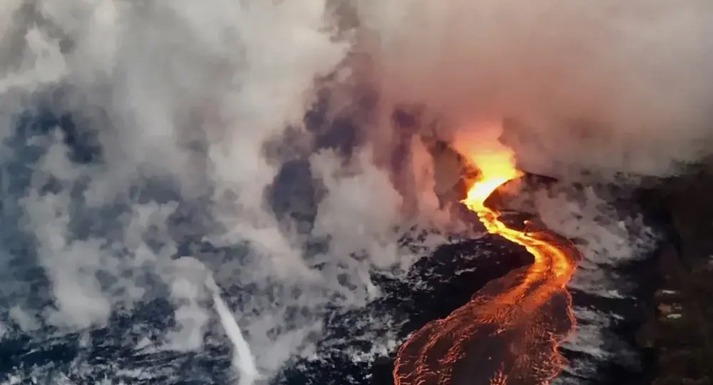 Glowing lava flowing into ocean creating steam on dark rocky shore