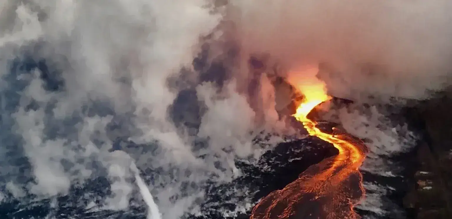 Glowing lava flowing into ocean creating steam on dark rocky shore