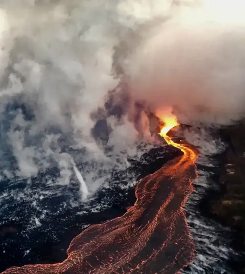 Glowing lava flowing into ocean creating steam on dark rocky shore