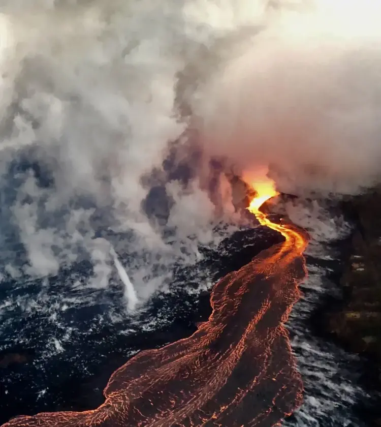 Glowing lava flowing into ocean creating steam on dark rocky shore