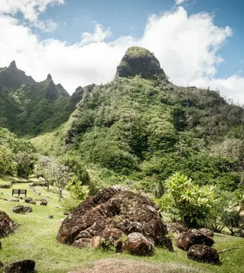 Lush green mountainous landscape with scattered large rocks and partly cloudy sky