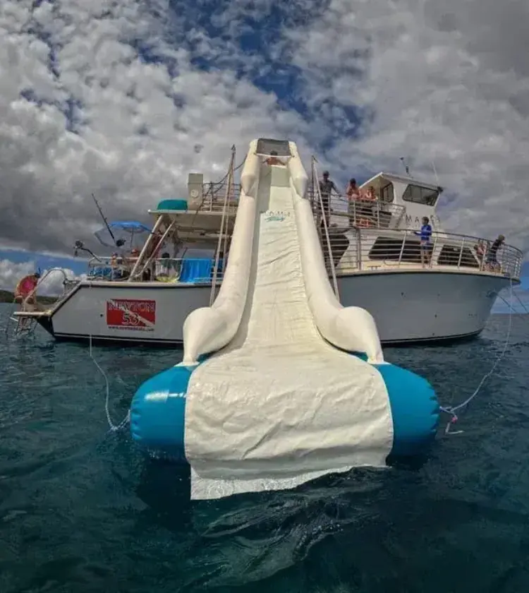 inflatable water slide descending into ocean from white boat with people on deck