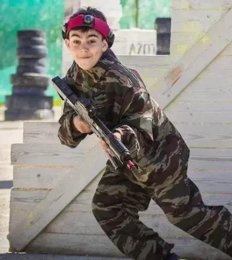 boy in camouflage playing paintball behind wooden barrier
