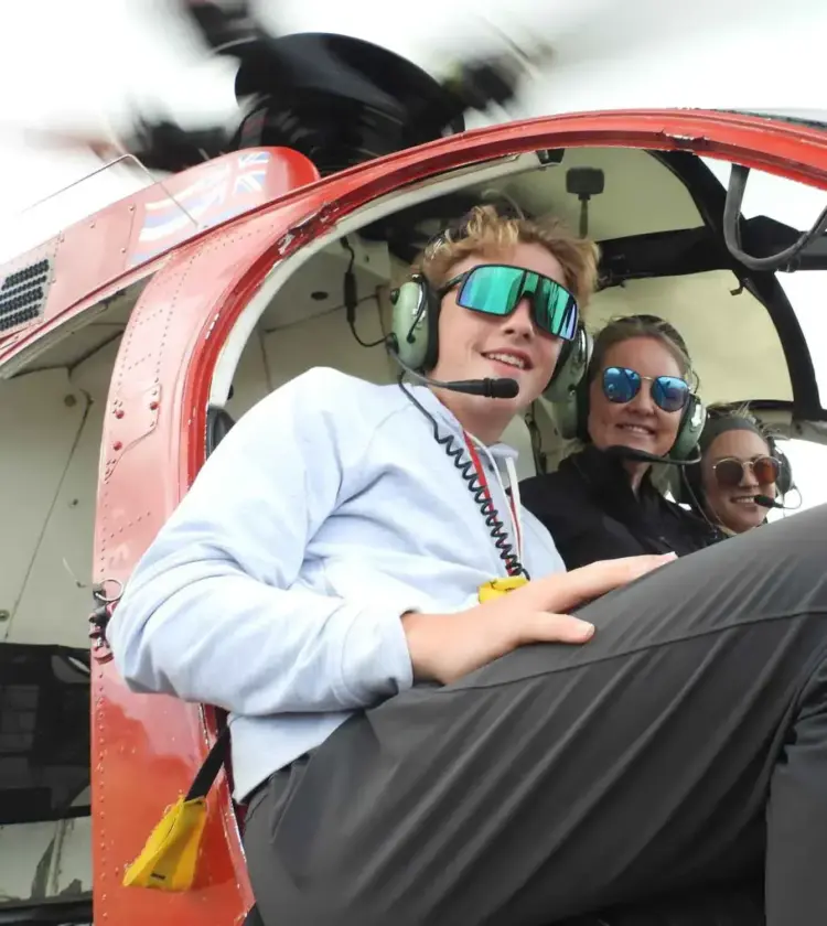 Three people wearing headsets and sunglasses sitting inside a helicopter cockpit smiling