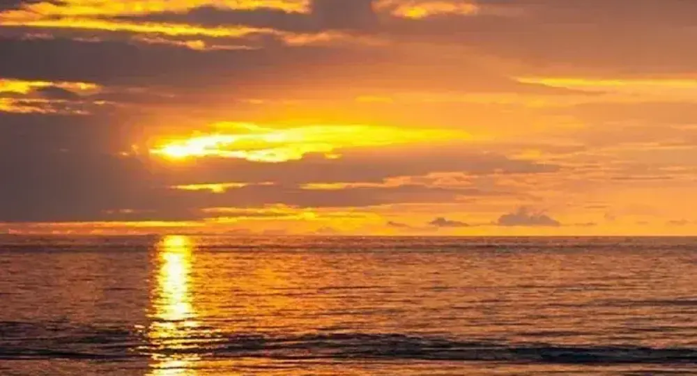 Golden sunset over ocean with bright sun reflection on water and partly cloudy sky