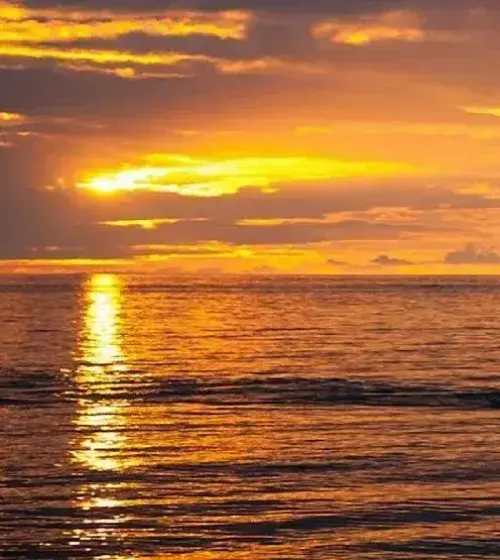 Golden sunset over ocean with bright sun reflection on water and partly cloudy sky