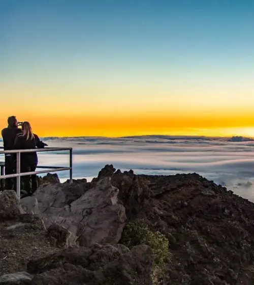 Couple observing sunset over clouds from volcanic summit ridge