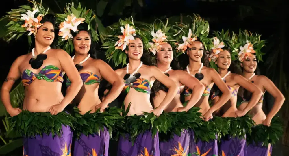 Row of hula dancers wearing green leaf skirts and flower headdresses performing on stage