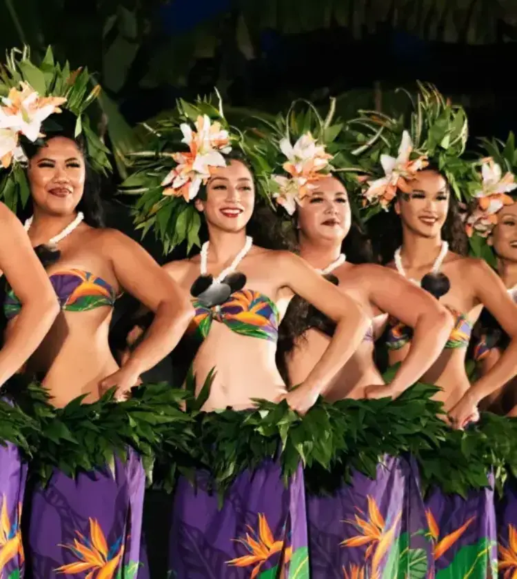 Row of hula dancers wearing green leaf skirts and flower headdresses performing on stage