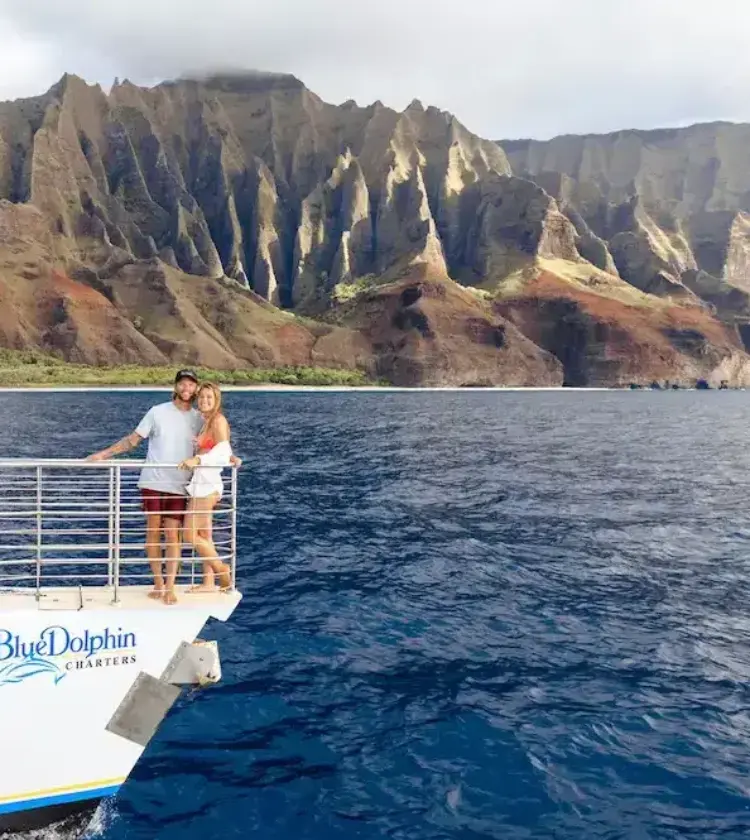 couple standing on boat deck with ocean and dramatic mountain cliffs in background