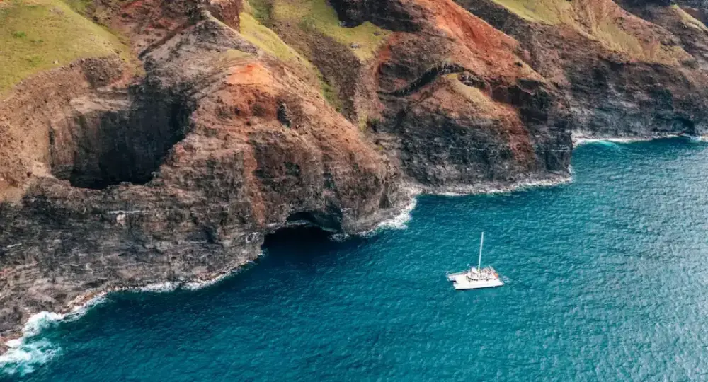 Boat sailing near steep rocky cliffs with ocean waves