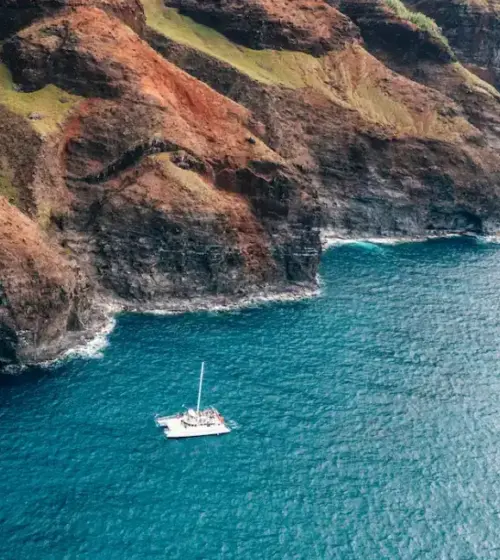 Boat sailing near steep rocky cliffs with ocean waves