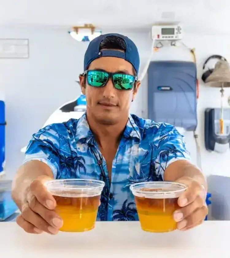 man wearing blue cap and sunglasses serving two plastic cups with drinks on boat