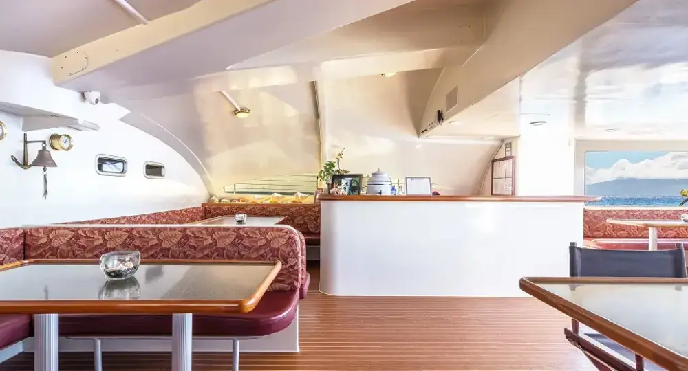 interior seating area on a boat with upholstered benches and glass tables looking out to the ocean