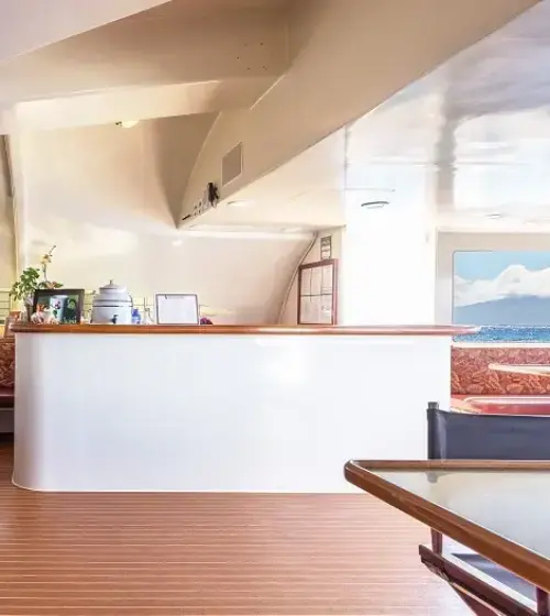 interior seating area on a boat with upholstered benches and glass tables looking out to the ocean