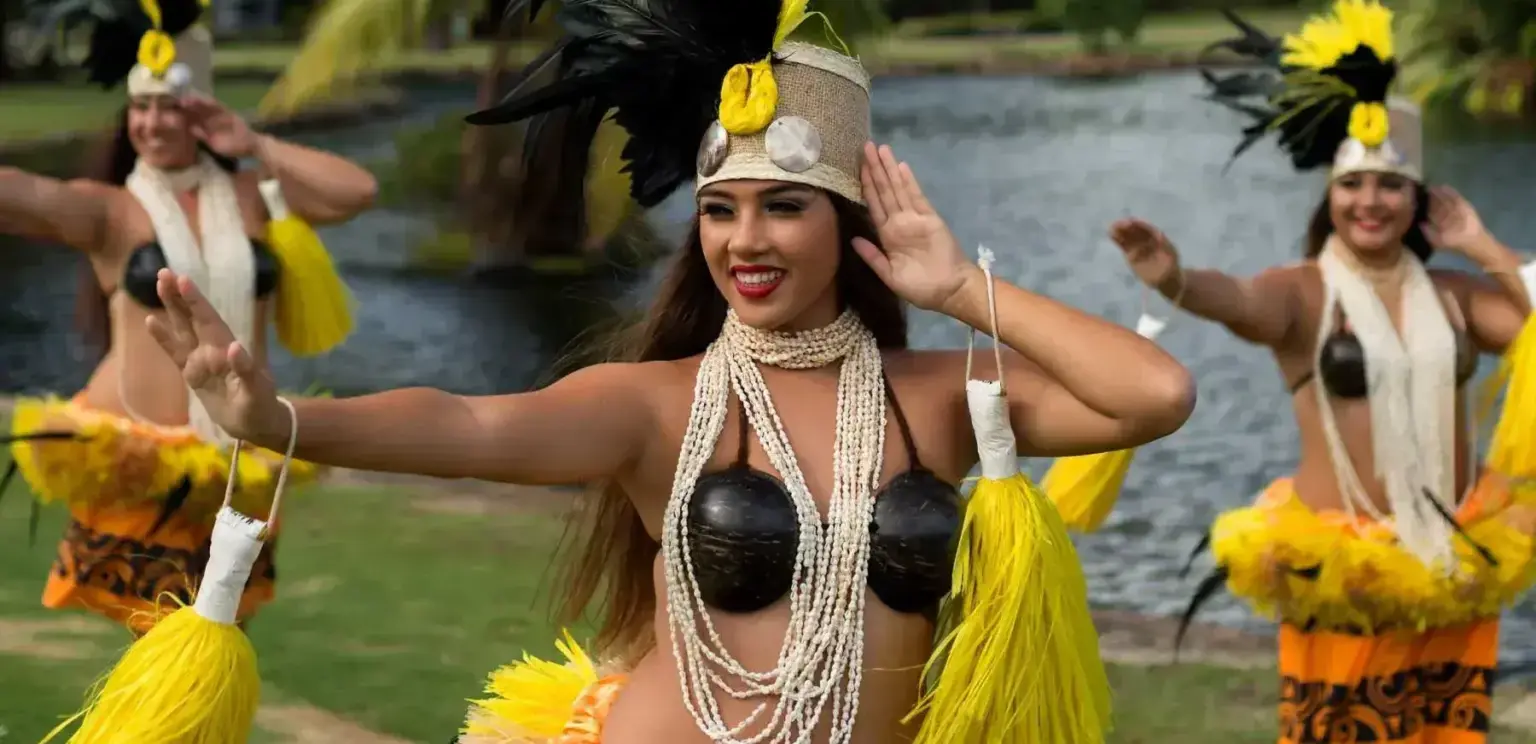 Hawaiian dancers dressed in traditional attire performing a dance near water