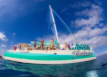 Sailing catamaran Teralani 4 with people on deck under blue sky and partly cloudy weather