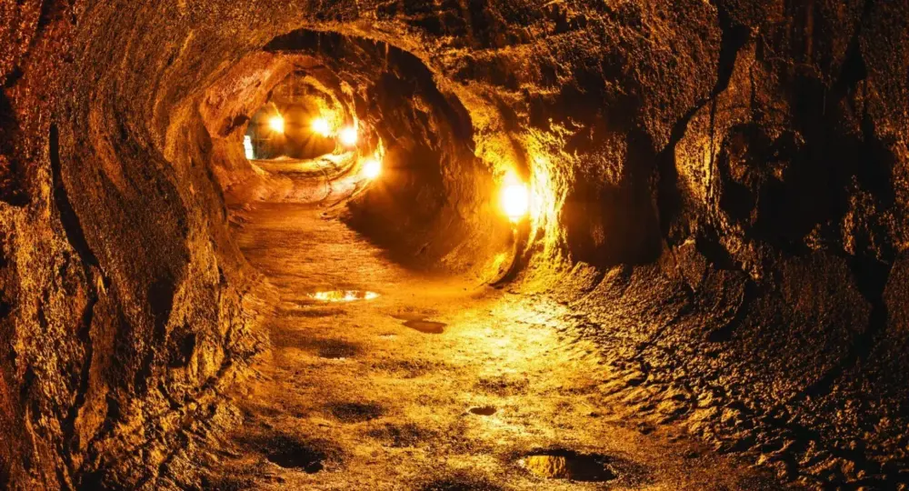Interior of illuminated lava tube cave with textured walls and puddles on the floor