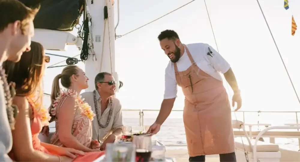 Chef serving food to happy guests on a yacht during sunset