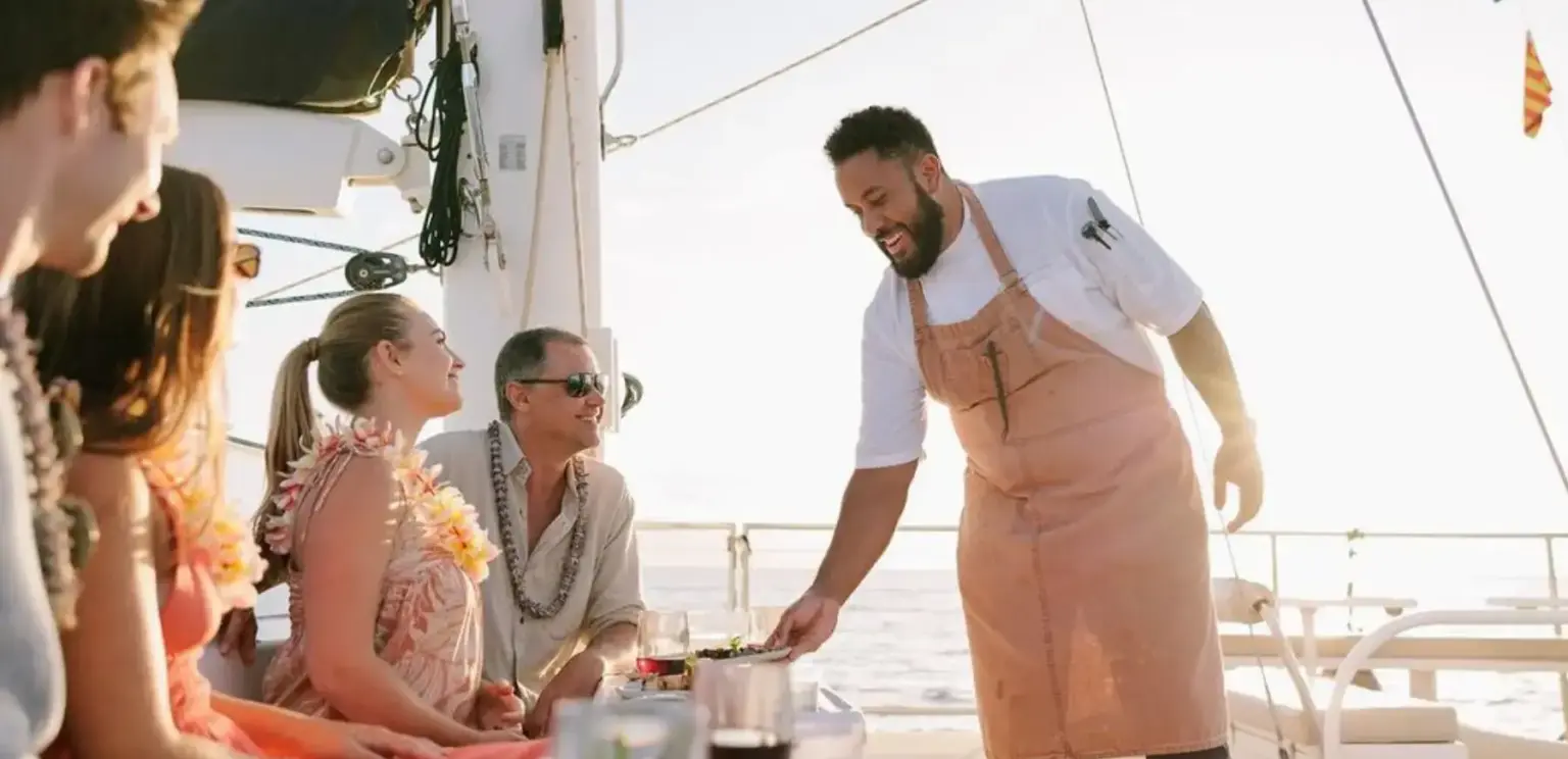 Chef serving food to happy guests on a yacht during sunset