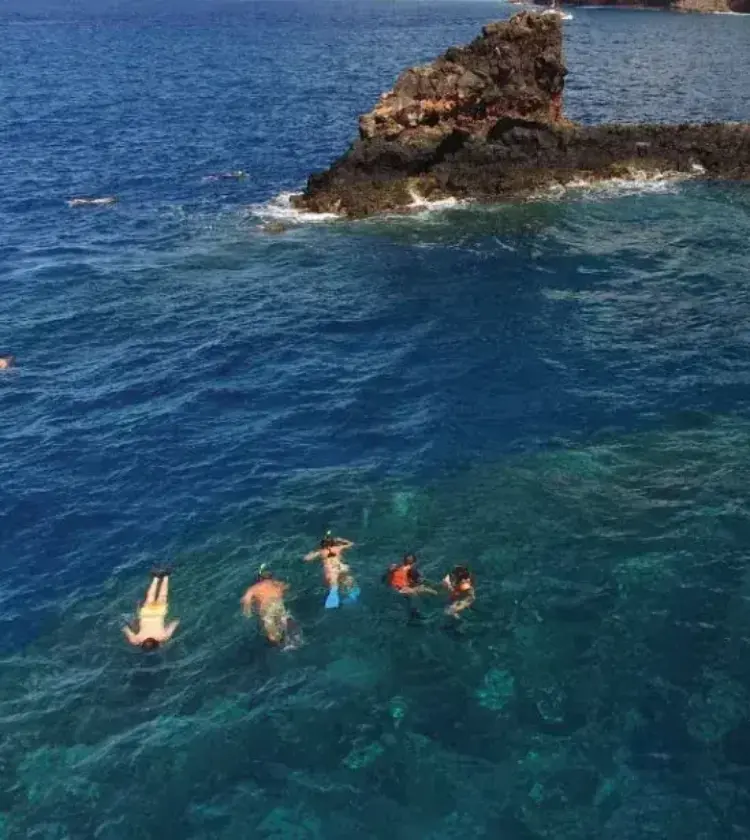 snorkelers swimming near rock formation in clear ocean water around Maui Hawaii