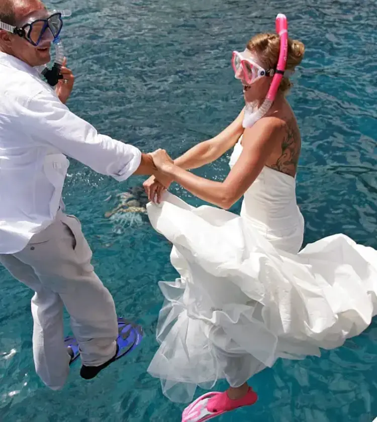 Couple in wedding dress and shirt with snorkeling gear jumping into clear blue ocean