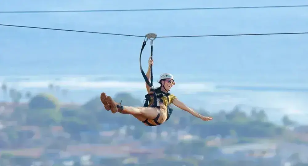 person ziplining over a coastal town with ocean in background