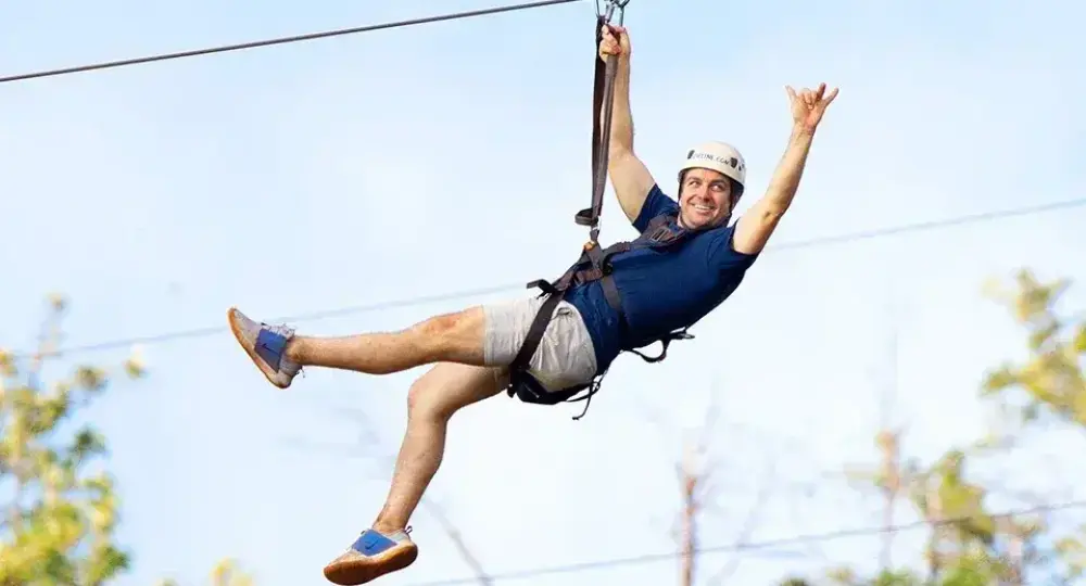 man wearing helmet and harness ziplining over trees