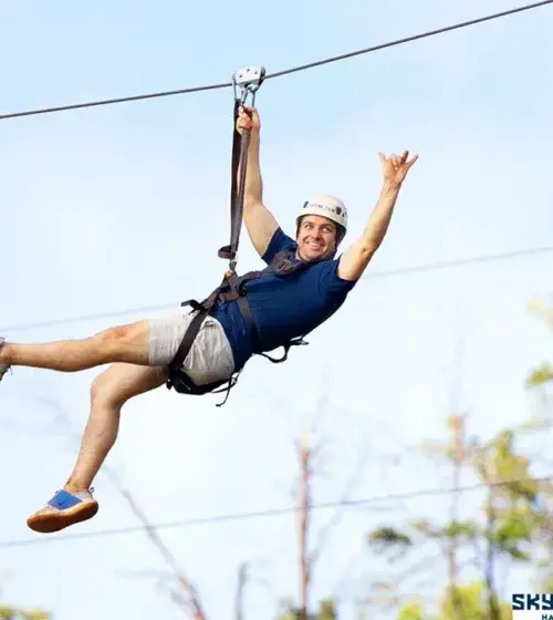 man wearing helmet and harness ziplining over trees