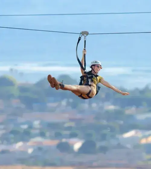 person ziplining over a coastal town with ocean in background
