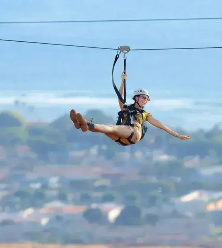 person ziplining over a coastal town with ocean in background
