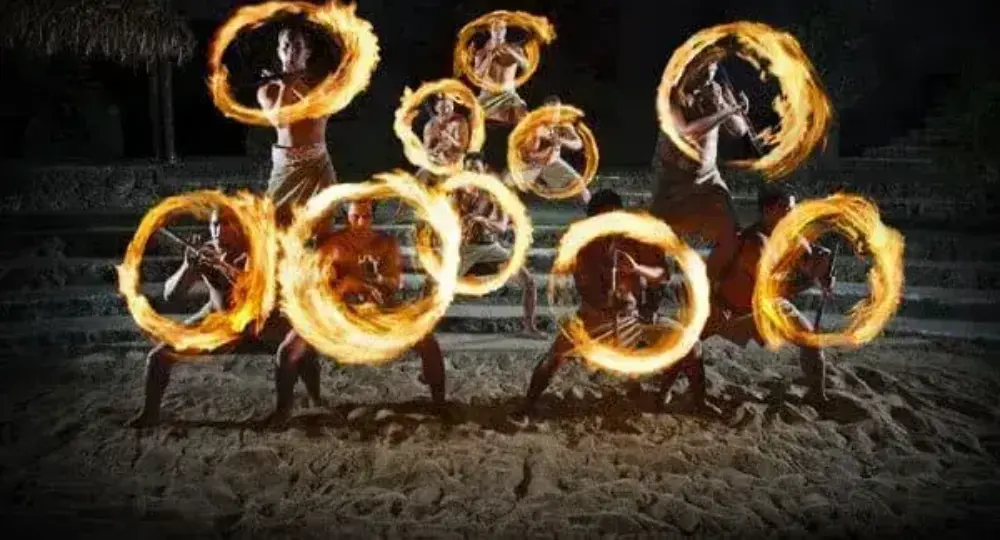 Nighttime Hawaiian fire dancers performing with spinning fire rings on sandy ground