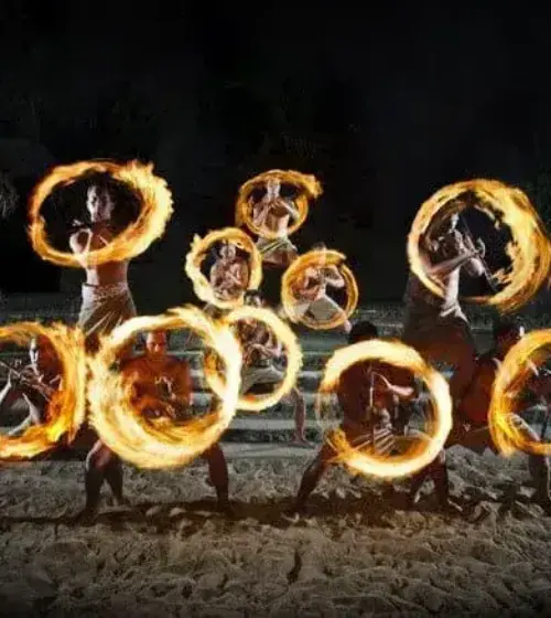 Nighttime Hawaiian fire dancers performing with spinning fire rings on sandy ground