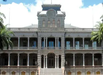 Historic government building with columns and palm trees on each side under a partly cloudy sky