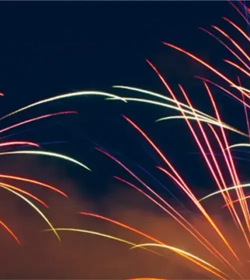 Multi-colored fireworks bursts glowing in the night sky with smoke below