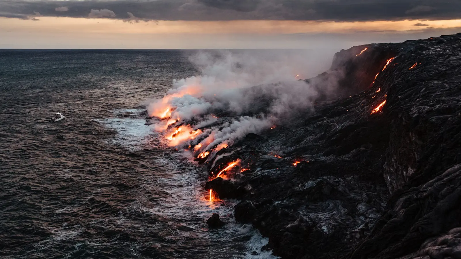 lava flowing into ocean at rocky coastline with smoke and glowing molten rock at sunset