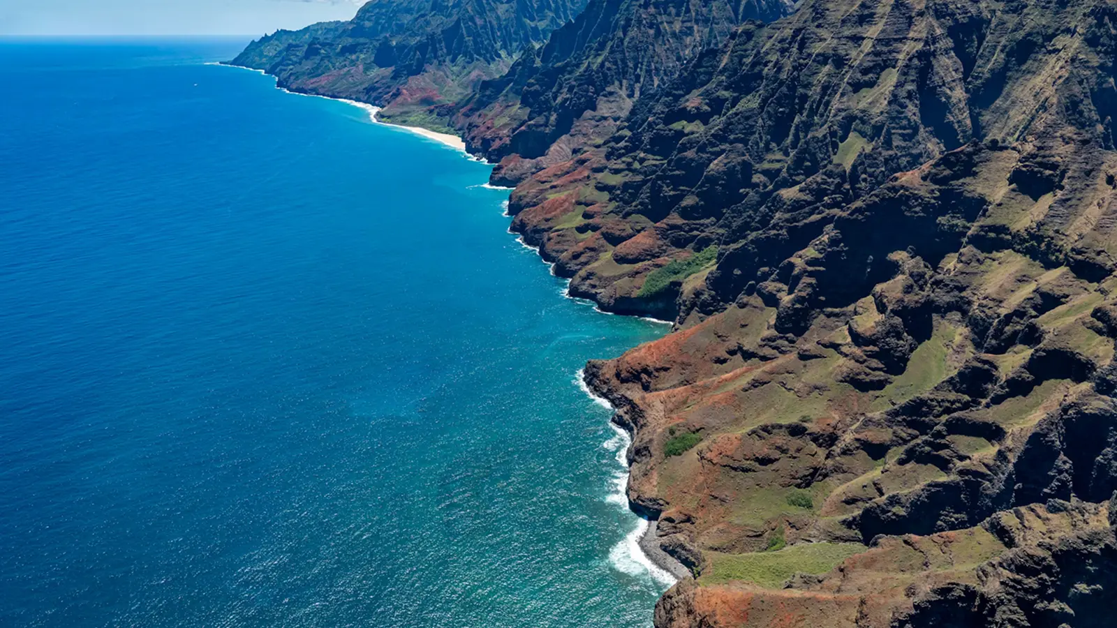 Aerial view of the blue ocean along steep cliffs of the Na Pali Coast with sunlight sparkling on the water