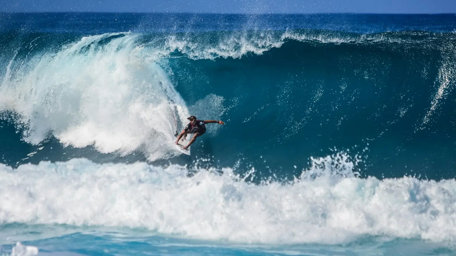 Surfer riding a large blue wave with white water spray in the ocean