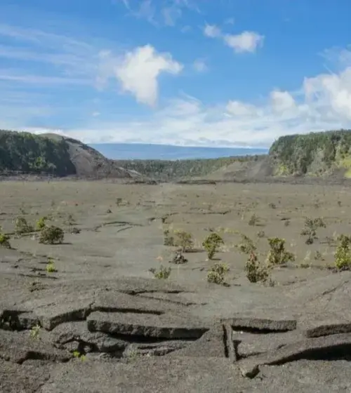 Volcanic crater with small bushes under a partly cloudy sky