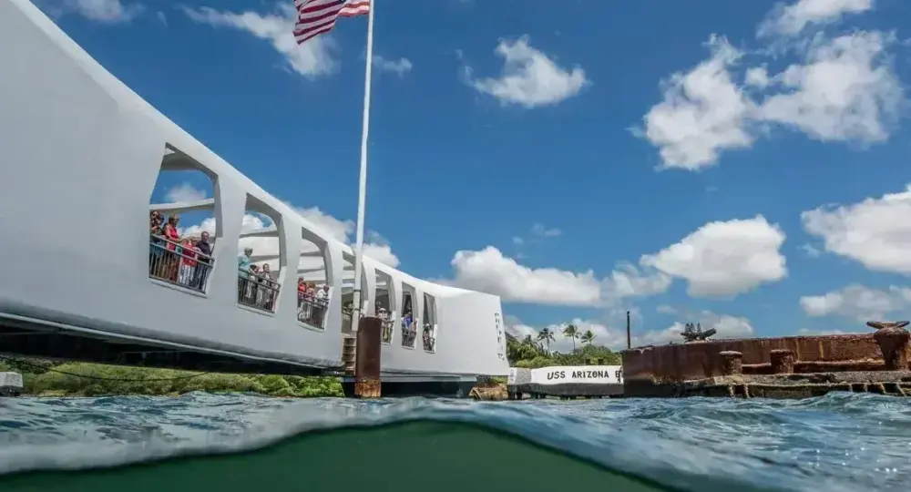 USS Arizona Memorial with American flag and visitors on a sunny day under blue sky with scattered clouds