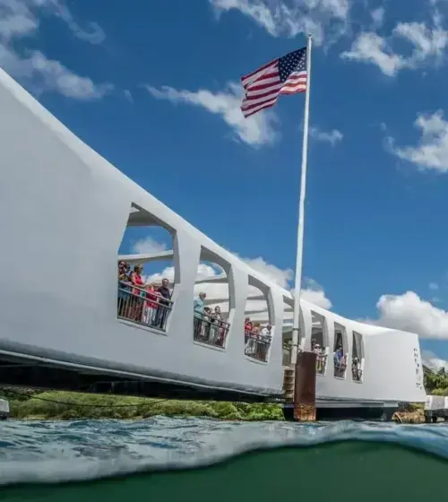 USS Arizona Memorial with American flag and visitors on a sunny day under blue sky with scattered clouds