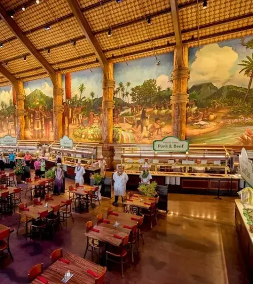 Spacious indoor dining area with wooden tables and chairs under a high ceiling featuring a large mural depicting Hawaiian scenes