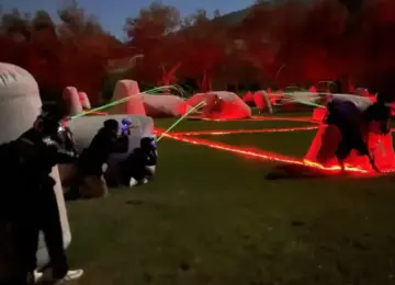 people playing laser tag outdoors at night with red and green laser lights