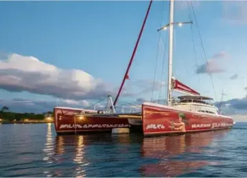 red sailing catamaran on calm ocean water with partly cloudy sky at sunset