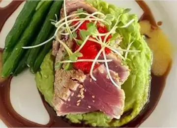 seared ahi tuna on green pea puree with green beans and sauce on a white plate