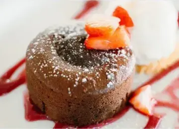 Chocolate lava cake topped with powdered sugar and strawberry pieces on a plate with red sauce