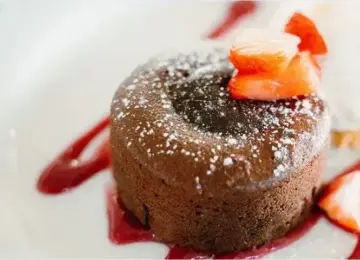 chocolate lava cake with powdered sugar topping and sliced strawberries on a white plate with red sauce