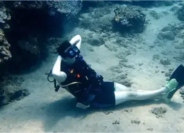 scuba diver resting on ocean floor near coral formations