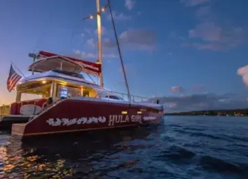Red Hula Girl catamaran boat on ocean at sunset with American flag and colorful sky